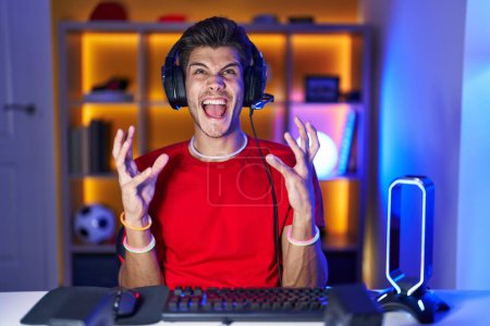 Téléchargez les photos : Young hispanic man playing video games crazy and mad shouting and yelling with aggressive expression and arms raised. frustration concept. - en image libre de droit