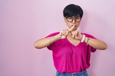 Téléchargez les photos : Jeune femme asiatique aux cheveux courts debout sur fond rose expression de rejet en croisant les doigts faisant signe négatif - en image libre de droit