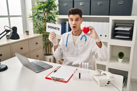 Téléchargez les photos : Young hispanic doctor man supporting organs donations in shock face, looking skeptical and sarcastic, surprised with open mouth - en image libre de droit