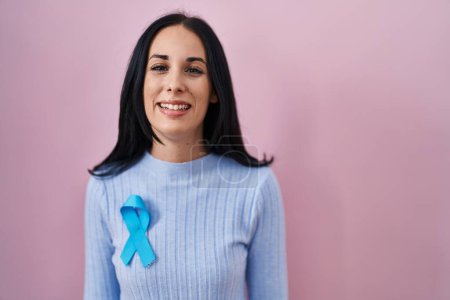 Foto de Mujer hispana vistiendo cinta azul con aspecto positivo y feliz de pie y sonriendo con una sonrisa confiada mostrando los dientes - Imagen libre de derechos