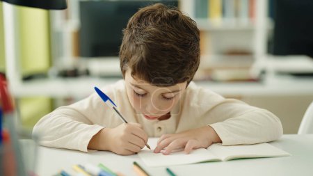 Foto de Adorable hispanic boy student writing on notebook at classroom - Imagen libre de derechos