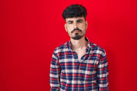 Photo for Young hispanic man with beard standing over red background looking sleepy and tired, exhausted for fatigue and hangover, lazy eyes in the morning. - Royalty Free Image