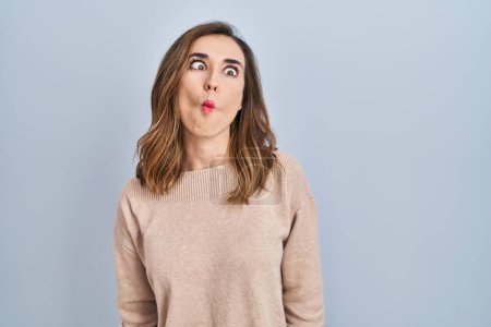 Foto de Young woman standing over isolated background making fish face with lips, crazy and comical gesture. funny expression. - Imagen libre de derechos