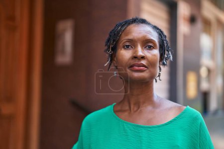 Téléchargez les photos : Moyen Age femme afro-américaine debout avec une expression sérieuse dans la rue - en image libre de droit