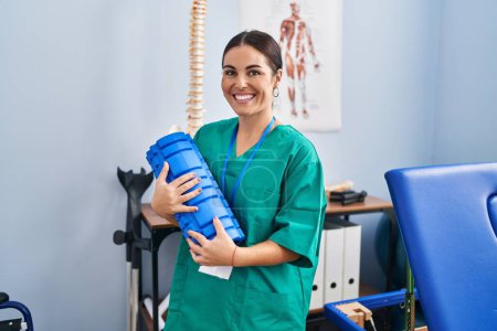 Foto de Young beautiful hispanic woman physiotherapist smiling confident holding foam roller at rehab clinic - Imagen libre de derechos
