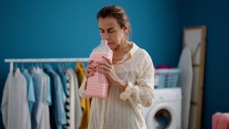 Photo for Middle age hispanic woman smelling detergent at laundry room - Royalty Free Image