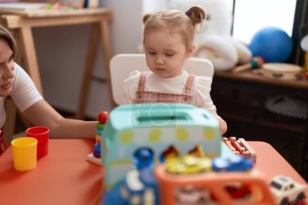 Foto de Maestro y niño pequeño sentado en la mesa jugando con juguetes en el jardín de infantes - Imagen libre de derechos