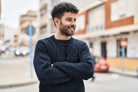 Téléchargez les photos : Jeune homme arabe souriant confiant debout avec les bras croisés geste à la rue - en image libre de droit