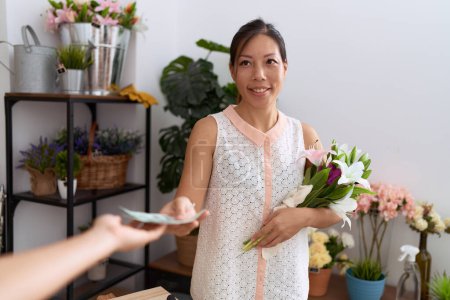 Foto de Young asian woman customer holding bouquet of flowers paying with dollars at flower shop - Imagen libre de derechos