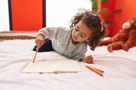 Photo for Adorable hispanic girl drawing on notebook lying on sofa at bedroom - Royalty Free Image