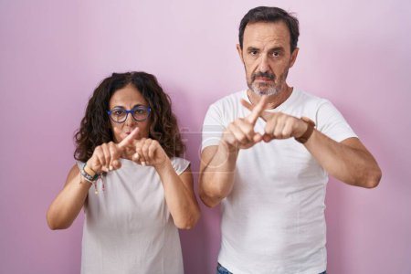 Téléchargez les photos : Middle age hispanic couple together over pink background rejection expression crossing fingers doing negative sign - en image libre de droit