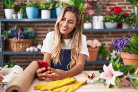 Photo for Young blonde woman florist smiling confident using smartphone at florist - Royalty Free Image