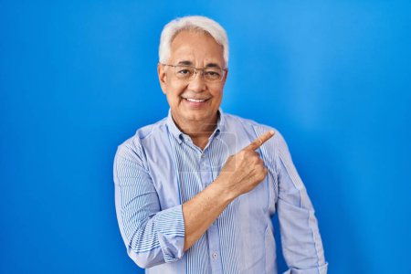 Photo for Hispanic senior man wearing glasses cheerful with a smile on face pointing with hand and finger up to the side with happy and natural expression - Royalty Free Image