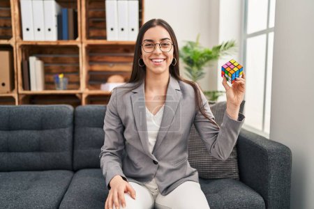 Foto de Hispanic woman playing colorful puzzle cube intelligence game looking positive and happy standing and smiling with a confident smile showing teeth - Imagen libre de derechos