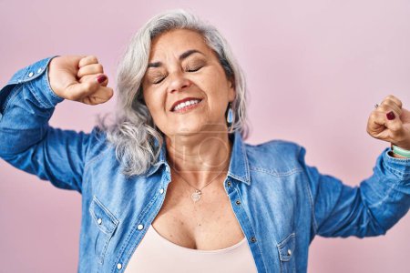 Photo for Middle age woman with grey hair standing over pink background stretching back, tired and relaxed, sleepy and yawning for early morning - Royalty Free Image