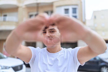 Téléchargez les photos : Non binary man smiling confident doing heart gesture with hands at street - en image libre de droit