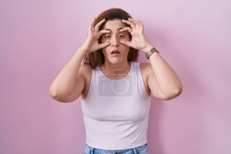 Photo for Brunette woman standing over pink background trying to open eyes with fingers, sleepy and tired for morning fatigue - Royalty Free Image