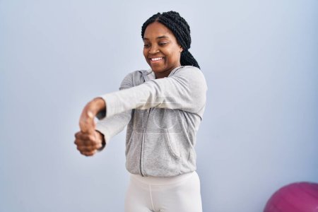 Foto de Mujer afroamericana sonriendo confiada estirando el brazo en el centro deportivo - Imagen libre de derechos