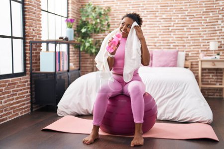 Foto de Mujer afroamericana bebiendo agua usando toalla en el dormitorio - Imagen libre de derechos