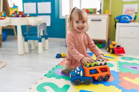 Téléchargez les photos : Adorable blonde girl smiling confident playing with car toys at kindergarten - en image libre de droit
