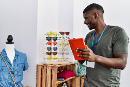 Foto de Young african american man smiling confident using touchpad working at clothing store - Imagen libre de derechos