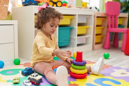Photo for Adorable hispanic toddler playing with hoops toy sitting on floor at kindergarten - Royalty Free Image