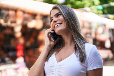 Téléchargez les photos : Jeune femme souriant confiant parler sur le smartphone au marché de la rue - en image libre de droit