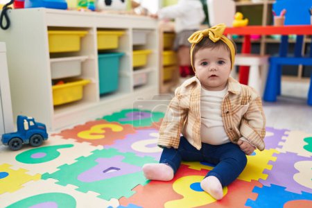 Photo for Adorable blonde toddler sitting on floor with serious expression at kindergarten - Royalty Free Image
