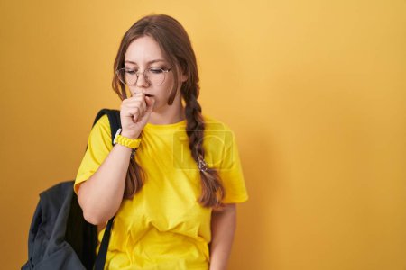 Téléchargez les photos : Jeune femme caucasienne portant un sac à dos étudiant sur fond jaune se sentant mal à l'aise et toussant comme symptôme de rhume ou de bronchite. concept de soins de santé. - en image libre de droit