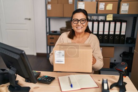 Téléchargez les photos : Middle age hispanic woman ecommerce business worker holding package at office - en image libre de droit