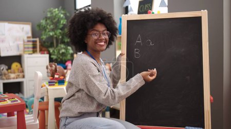 Photo for African american woman teacher smiling confident writing on blackboard at kindergarten - Royalty Free Image