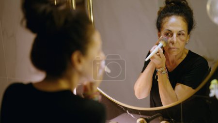 Téléchargez les photos : Middle age hispanic woman using makeup to cover signs of domestic violence at bathroom - en image libre de droit