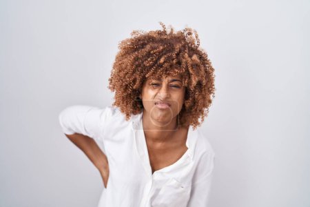 Foto de Young hispanic woman with curly hair standing over white background suffering of backache, touching back with hand, muscular pain - Imagen libre de derechos