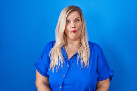 Photo for Caucasian plus size woman standing over blue background making fish face with lips, crazy and comical gesture. funny expression. - Royalty Free Image