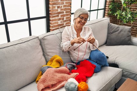 Foto de Mujer de mediana edad tejiendo en extremos sentado en el sofá en casa - Imagen libre de derechos