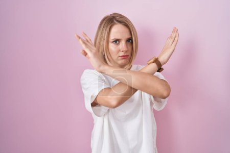 Photo for Young caucasian woman standing over pink background rejection expression crossing arms doing negative sign, angry face - Royalty Free Image