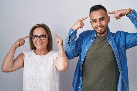 Photo for Hispanic mother and son standing together smiling pointing to head with both hands finger, great idea or thought, good memory - Royalty Free Image