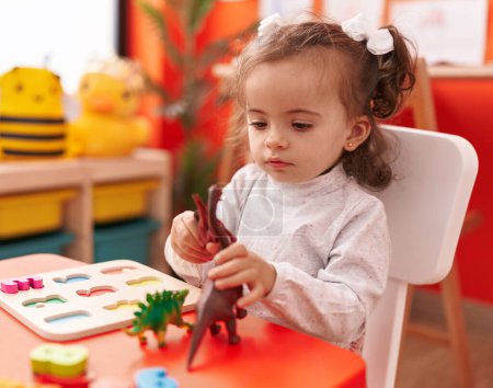 Foto de Adorable niño hispano jugando con dino juguete sentado en la mesa en el jardín de infantes - Imagen libre de derechos