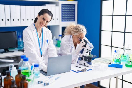 Photo for Two women scientists using microscope and laptop at laboratory - Royalty Free Image