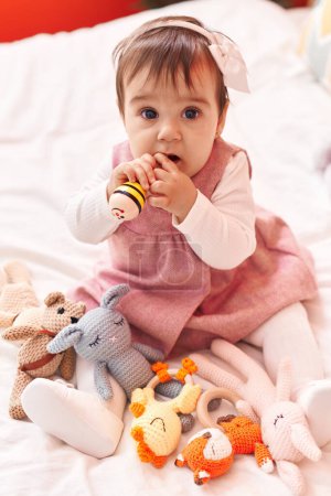 Photo for Adorable hispanic baby bitting maraca sitting on bed at bedroom - Royalty Free Image