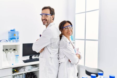 Téléchargez les photos : Hommes et femmes d'âge moyen portant l'uniforme de scientifique debout les bras croisés au laboratoire - en image libre de droit