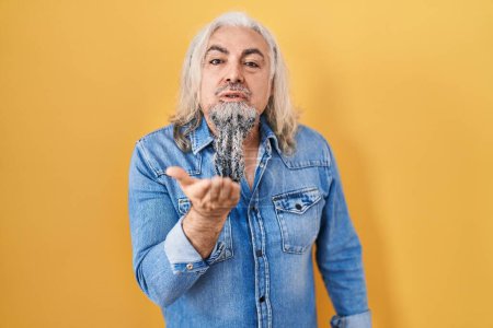 Photo for Middle age man with grey hair standing over yellow background looking at the camera blowing a kiss with hand on air being lovely and sexy. love expression. - Royalty Free Image