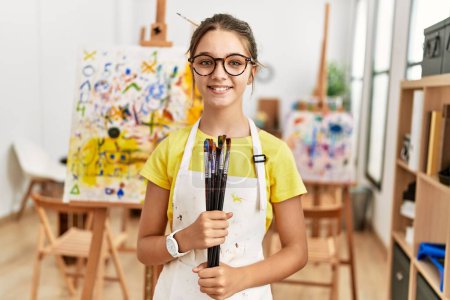 Photo for Adorable girl smiling confident holding paintbrushes at art studio - Royalty Free Image