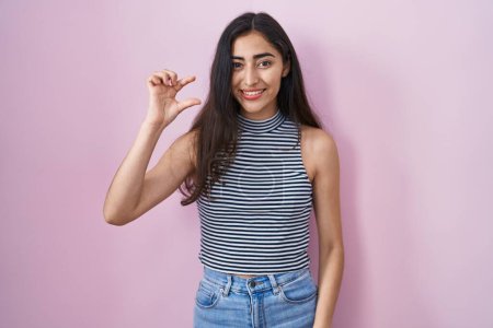 Téléchargez les photos : Young teenager girl wearing casual striped t shirt smiling and confident gesturing with hand doing small size sign with fingers looking and the camera. measure concept. - en image libre de droit