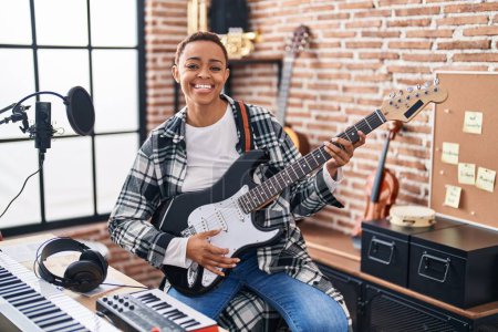 Foto de Mujer afroamericana músico sonriendo confiado tocando la guitarra eléctrica en el estudio de música - Imagen libre de derechos