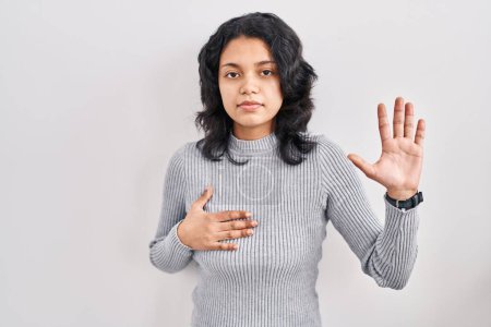 Téléchargez les photos : Hispanic woman with dark hair standing over isolated background swearing with hand on chest and open palm, making a loyalty promise oath - en image libre de droit