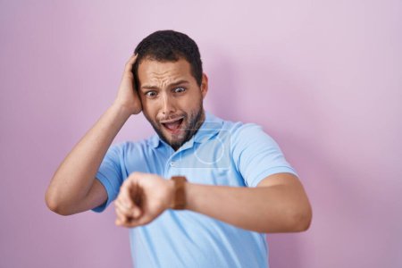 Photo for Hispanic man standing over pink background looking at the watch time worried, afraid of getting late - Royalty Free Image