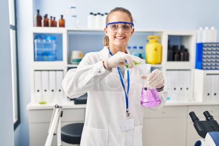 Foto de Young blonde woman wearing scientist uniform pouring liquid on test tube at laboratory - Imagen libre de derechos