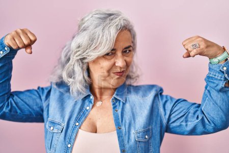 Photo for Middle age woman with grey hair standing over pink background showing arms muscles smiling proud. fitness concept. - Royalty Free Image
