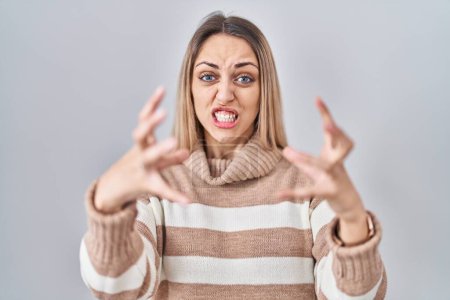 Photo for Young blonde woman wearing turtleneck sweater over isolated background shouting frustrated with rage, hands trying to strangle, yelling mad - Royalty Free Image